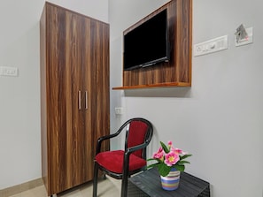 A room with a wooden wardrobe, a television mounted on the wall, a red chair, and a potted plant. - Townhouse swaroop inn (Lucknow)