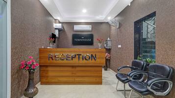 A reception desk with a sign that reads 'RECEPTION' and 'TOWNHOUSE'. There are two chairs to the right of the desk, and a vase with flowers on the left.