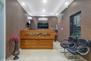 A reception desk with a sign that reads 'RECEPTION' and 'TOWNHOUSE'. There are two chairs to the right of the desk, and a vase with flowers on the left. - Townhouse swaroop inn (Lucknow)