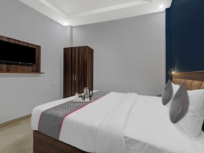 A hotel room with a bed, a television mounted on the wall, a wardrobe, and a bedside table with a kettle and cups. - Townhouse swaroop inn (Lucknow)