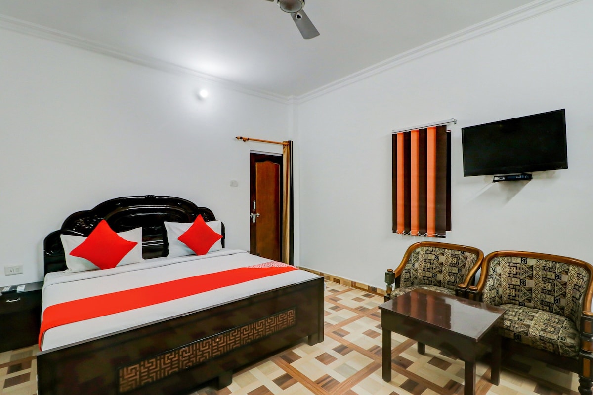 A hotel room with a bed, a television, a desk, and two patterned chairs.