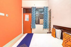 Una camera d'albergo con un letto, una finestra con tende, una porta e una parete con un interruttore della luce.