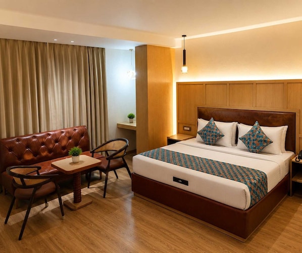 A hotel room with a large bed, a leather sofa, a small table, and a chair. - Deluxe King Room Maneraa Homes (Tirupati)