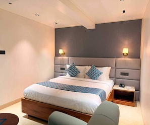A modern hotel room with a large bed, bedside tables, and a headboard with wall-mounted lights. - Deluxe King Room Maneraa Homes (Tirupati)