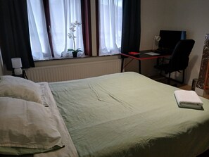 Habitació d'hotel amb llit, escriptori, cadira, televisió i finestra amb cortines.