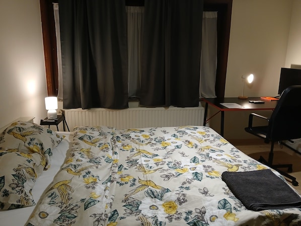 Een hotelkamer met een bed, een bureau met een computer, een stoel, een lamp en een raam met gordijnen.