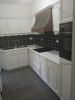 Een keuken met witte kasten, een zwart betegelde achterwand en een zwarte oven.