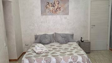 Un dormitorio con cama, mesitas de noche, un cuadro, una silla y una pequeña mesa.
