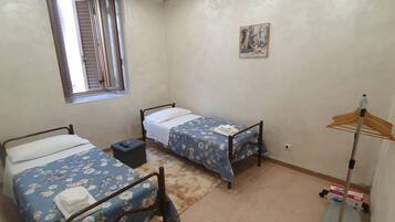 Ein Zimmer mit zwei Einzelbetten, einem Fenster, einem Bild an der Wand und einem Standventilator.