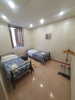 Una habitación con dos camas individuales, una ventana, un cuadro en la pared y un ventilador de pie.