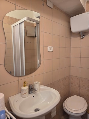 Une salle de bain avec un lavabo blanc, un miroir, des toilettes et un interrupteur fixé au mur.