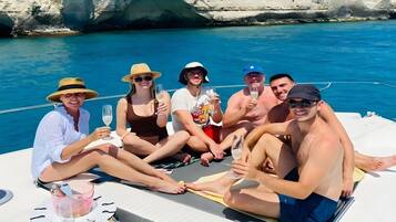 A group of people on a boat with a table and drinks, surrounded by water and a rocky coastline.