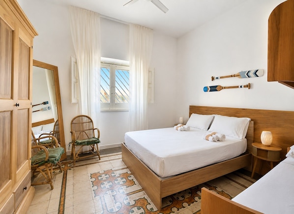 Ein Schlafzimmer mit einem hölzernen Bett, einem Sessel, einem Spiegel und einem Fenster mit Vorhängen.