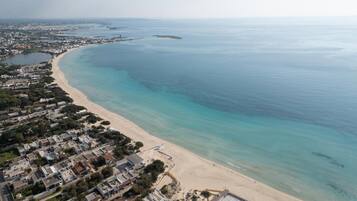 An aerial view of a coastal area with a beach, residential buildings, and a marina.