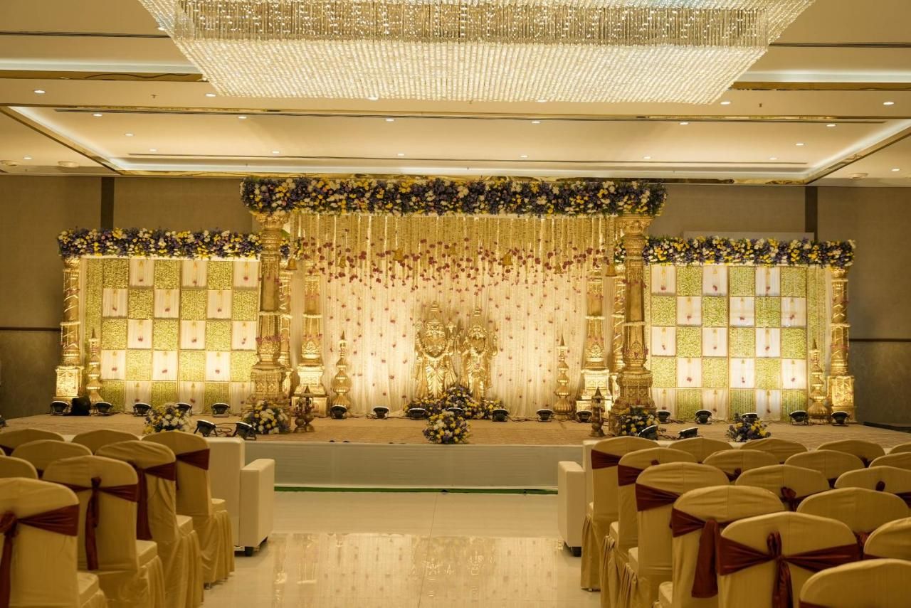 Ein festlicher Veranstaltungsraum mit Reihen von Stühlen, einer Bühne mit floralen Dekorationen und einer Kristallleuchtre.