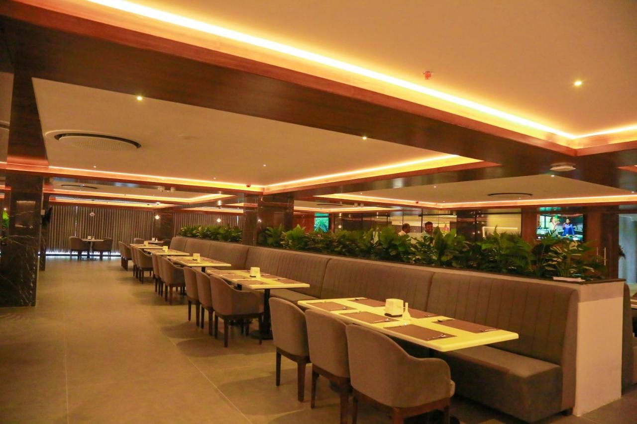 A modern restaurant with long communal tables and booths, ambient lighting, and a view of the cityscape.