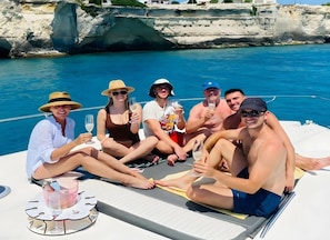 Eine Gruppe von Menschen auf einem Boot mit Tisch und Getränken, umgeben von Wasser und einer felsigen Küste.