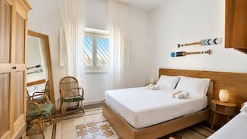 Ein Schlafzimmer mit einem hölzernen Bett, einem Sessel, einem Spiegel und einem Fenster mit Vorhängen.