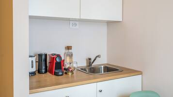 A kitchenette with a stainless steel sink, a red coffee maker, a white kettle, and a glass bottle.