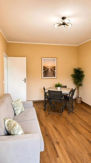 A room with a sofa, a dining table with chairs, a ceiling fan, a door, and a framed picture on the wall.