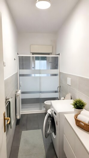 A modern bathroom with a shower, toilet, and washing machine.