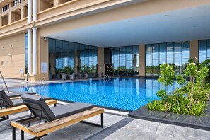 Piscina com espreguiçadeiras, área de estar coberta e vista para a fachada do edifício.