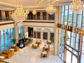 Um saguão de hotel com várias luminárias de cristal, área de bar, arranjos de assentos e grandes janelas com vista.