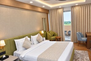 Quarto de hotel com uma cama grande, uma escrivaninha, uma cadeira, uma mesa pequena e vista para o exterior.
