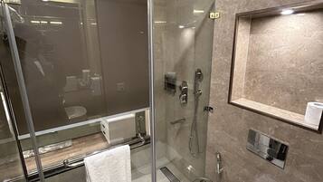 A modern bathroom with a glass-enclosed shower, a white sink, and a marble-tiled wall.