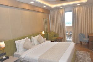 A hotel room with a large bed, a desk, a chair, and a view of the outdoors through the window. - Met City Club & Convention Centre (Yakubpur)
