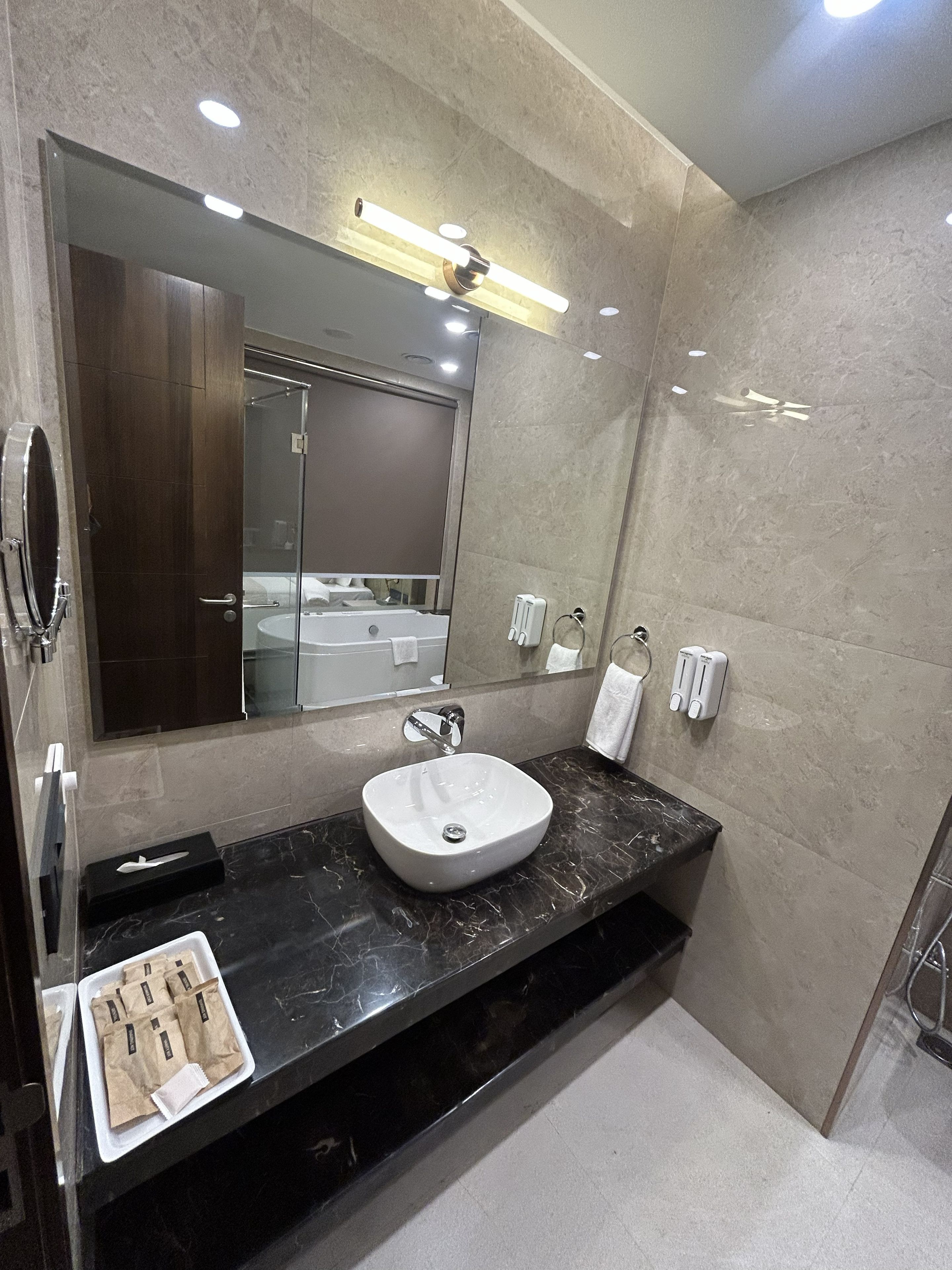 A modern bathroom with a large mirror, a white sink, and a dark marble countertop.