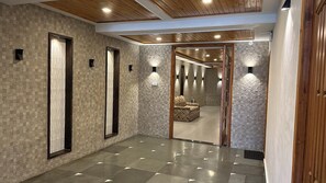 Un pasillo con suelo de baldosas, techo de madera y un muro espejado que refleja una habitación con un sofá estampado.