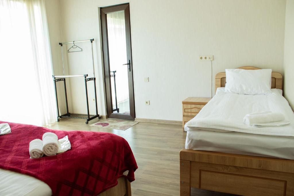 Une chambre d’hôtel avec deux lits, une tête de lit en bois, une couverture rouge et un porte-serviettes.