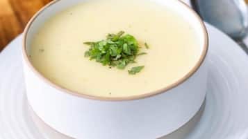 Un tazón de sopa cremosa sobre un plato blanco, con una cuchara, colocado sobre una mesa de madera.