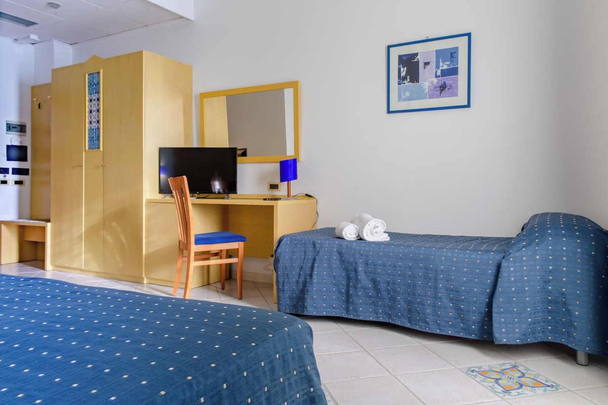 Une chambre d’hôtel avec deux lits, un bureau avec un ordinateur, une chaise, une télévision et un miroir fixé au mur.
