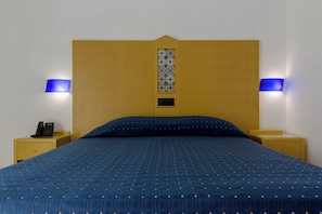 Un lit avec une tête de lit, deux lampes de chevet, une table de chevet avec un téléphone et un élément décoratif mural à motifs.