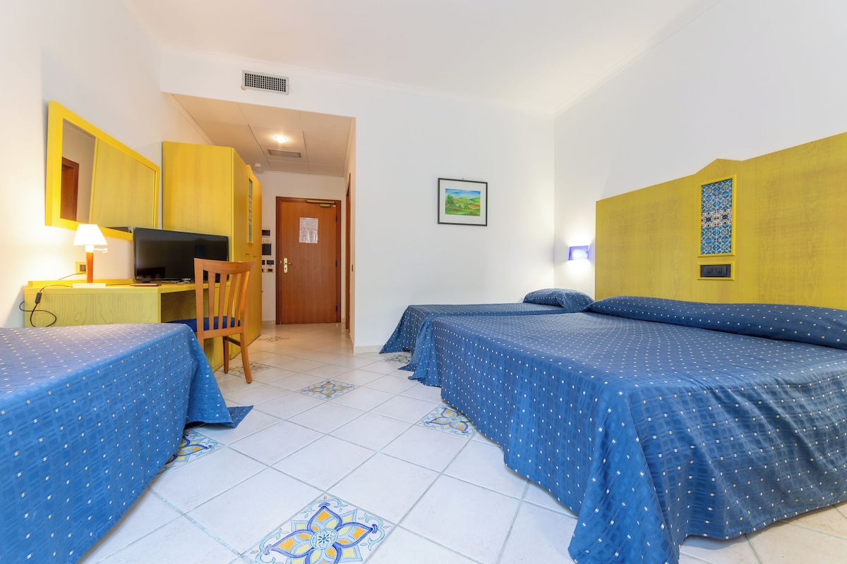 Une chambre d’hôtel avec deux lits, un bureau, une chaise, une télévision et une porte donnant sur une autre pièce.