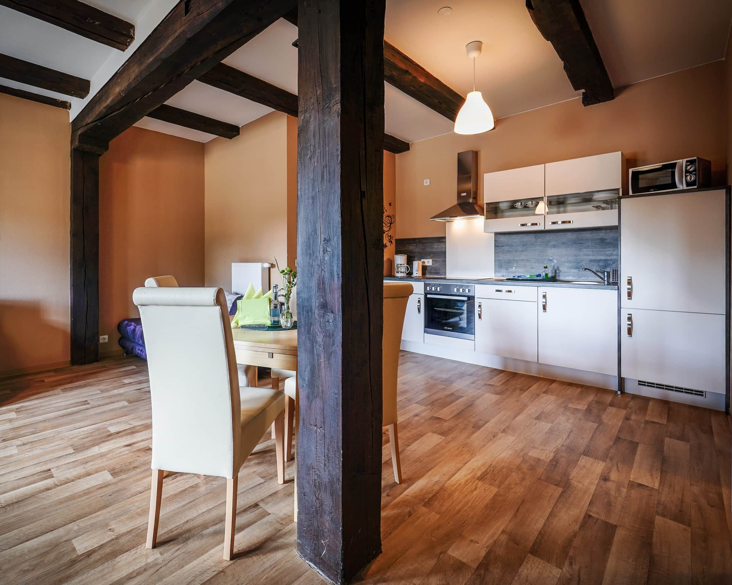 A modern kitchen with white cabinets, a microwave, and a stove. There is a dining area with a table and chairs.