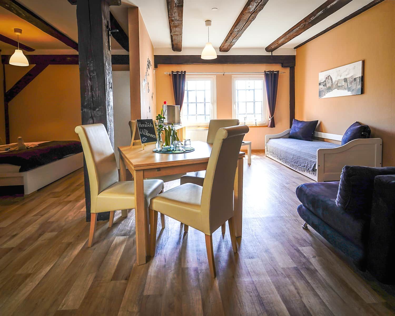 Een gezellige woonkamer met een eethoek, houten vloeren en een groot raam met gordijnen.