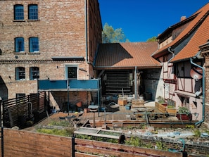Une cour avec une terrasse en bois, des bâtiments en briques et un toit recouvert de tuiles rouges.