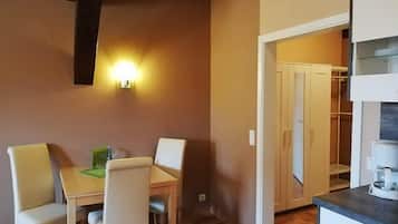 Un espace repas comprenant une table et des chaises, un luminaire fixé au mur, et un coin cuisine avec des placards et un plan de travail.