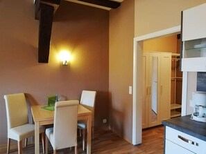 Een eetgedeelte met een tafel en stoelen, een wandlamp en een keuken met kasten en een aanrecht.