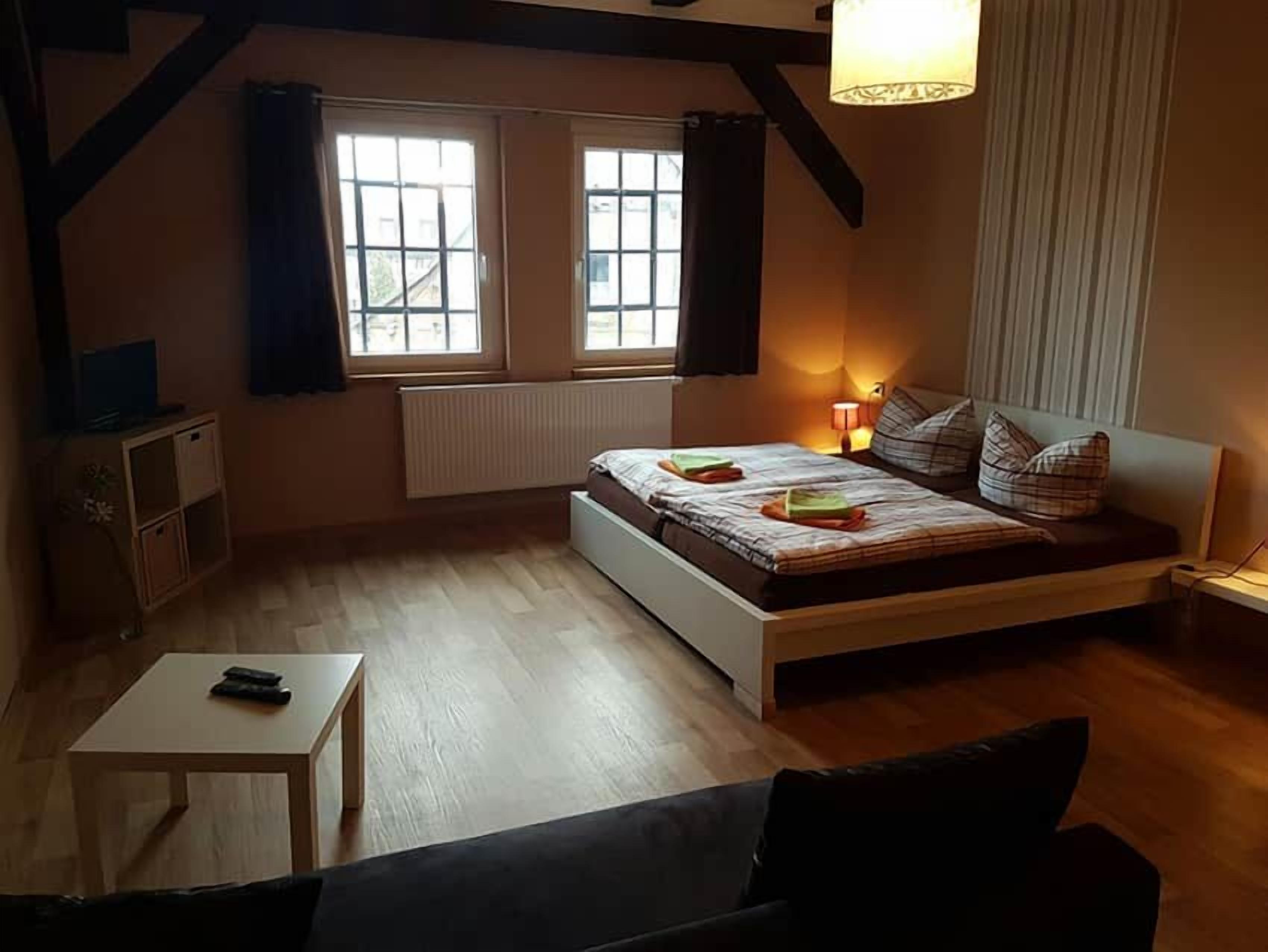 Ein Schlafzimmer mit einem Bett, einem Nachttisch, einer Lampe, einem Fenster und einer Heizung.