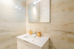 Un baño con un lavamanos blanco, dos dispensadores de jabón de madera, un espejo y una lámpara.