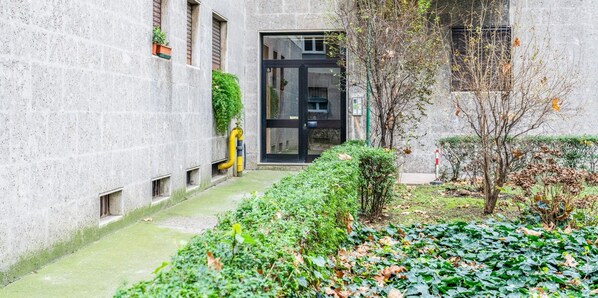 Une cour avec un bâtiment, un petit jardin et un tuyau jaune.