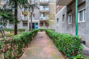 Un sendero bordeado por follaje y un edificio con varios balcones.