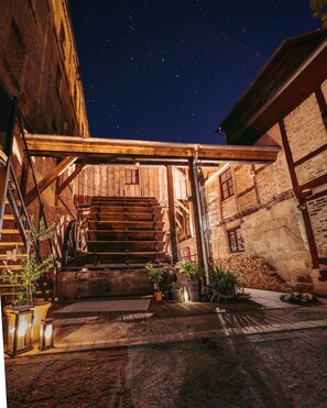 Eine rustikale Außentreppe führt zu einem Holzhaus, über dem sich ein sternenklarer Nachthimmel erstreckt.
