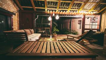 Una terraza rústica de madera con un banco, una mesa y un colgador de luces.