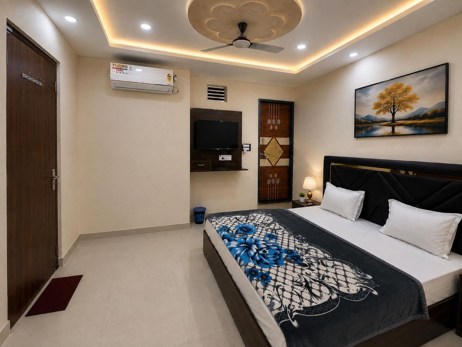 A hotel room with a bed, a TV, a ceiling fan, and a painting on the wall.