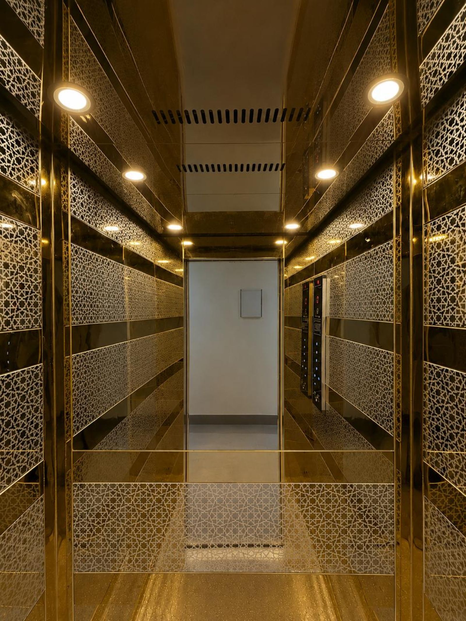 A modern elevator interior with patterned walls and ceiling lights.
